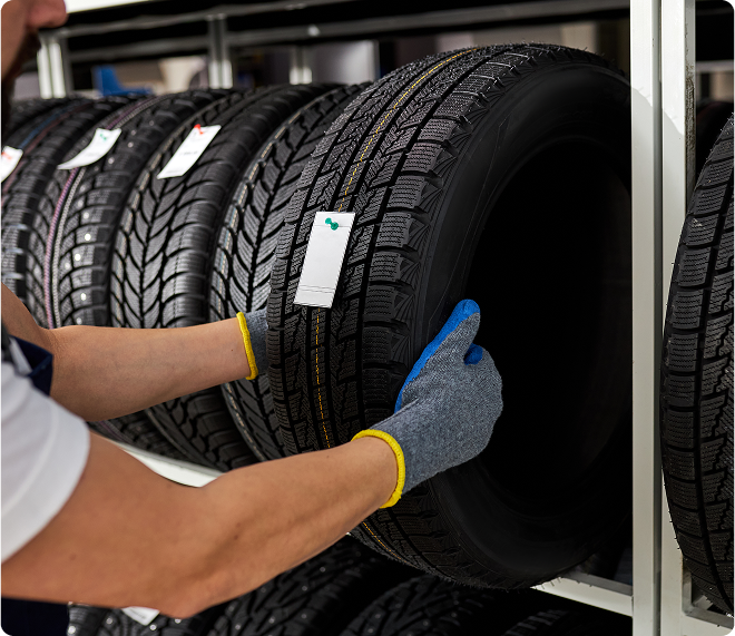 A person wearing gloves checks a tire's tread in a store display, with other tires on the rack.