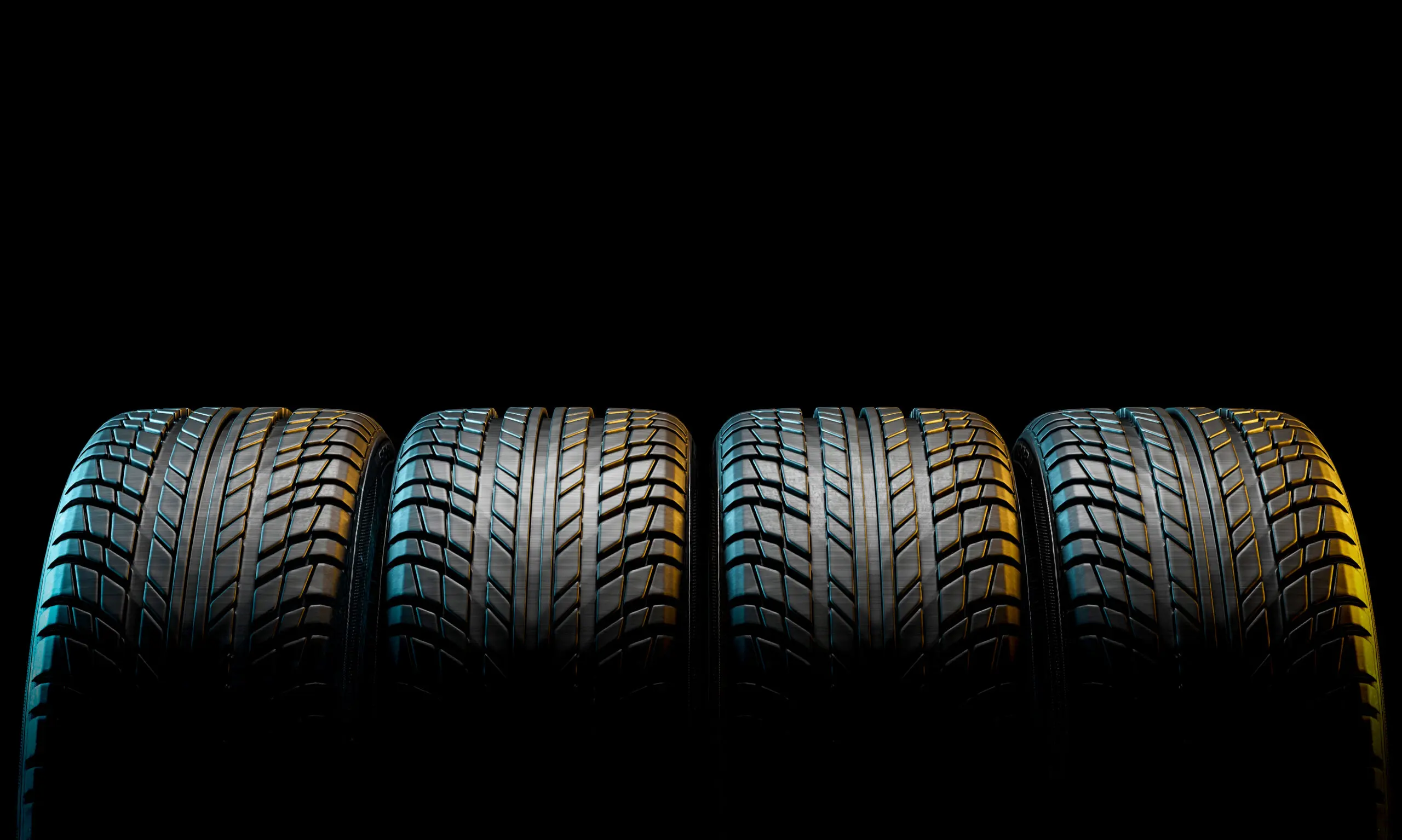 Four car tires standing side by side against a black background, showcasing their tread patterns.